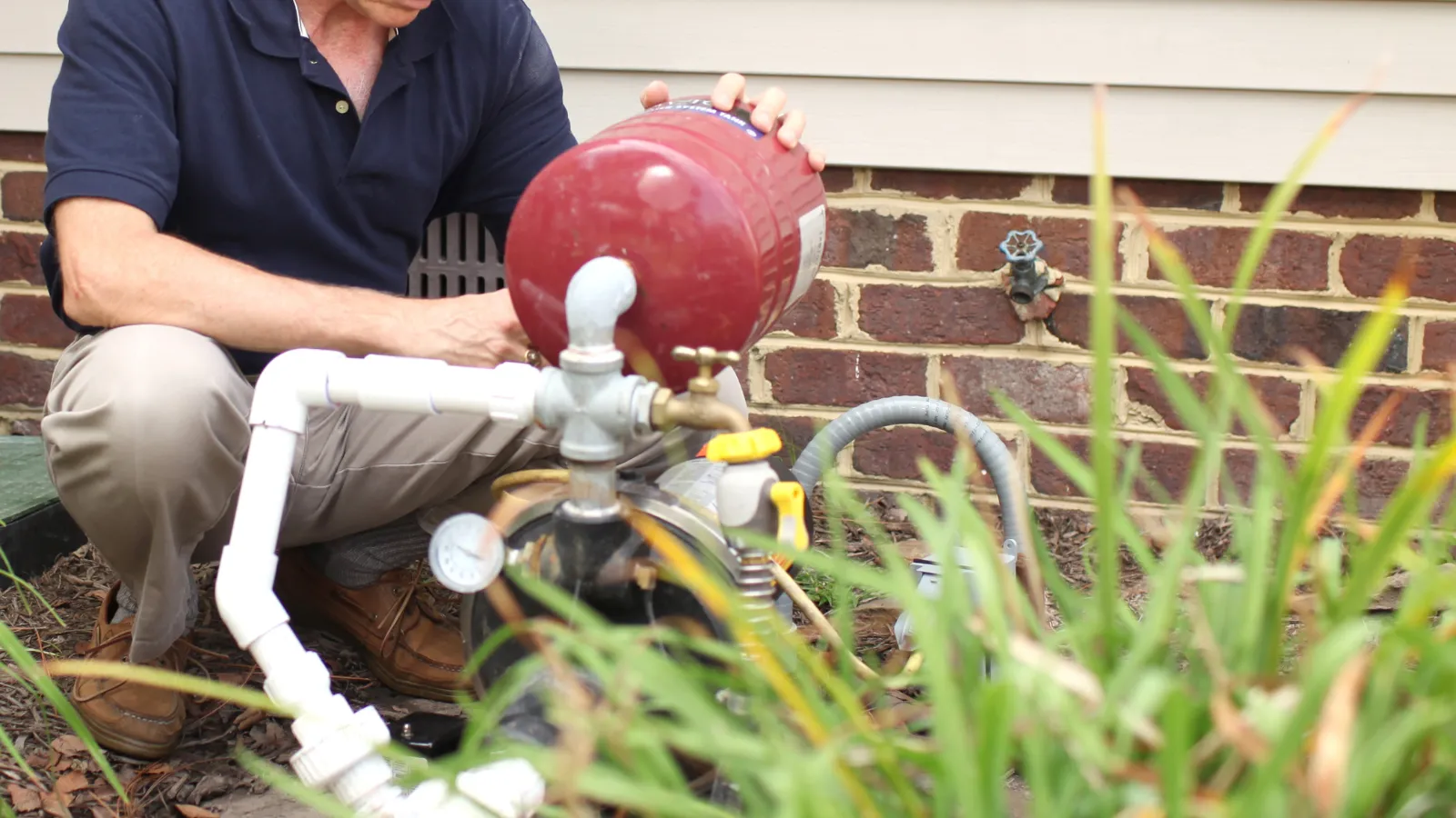 Technician servicing a well pump outside a home.