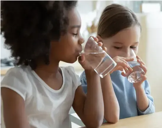 Two young children drinking clean water out of clear glasses.